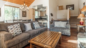 A spacious living room with a wooden ceiling, two grey sofas with patterned cushions, a wooden coffee table, and a staircase leading to an upper level. - Mammoth Gateway Village #1 - Updated Townhome-Walk To Village 3 Bed+Loft, Sleeps 10 Private Hot Tub (Mammoth Lakes)