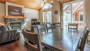 A spacious living room with a stone fireplace, a large dining table, and a cozy seating area. - Mammoth Gateway Village #1 - Updated Townhome-Walk To Village 3 Bed+Loft, Sleeps 10 Private Hot Tub (Mammoth Lakes)