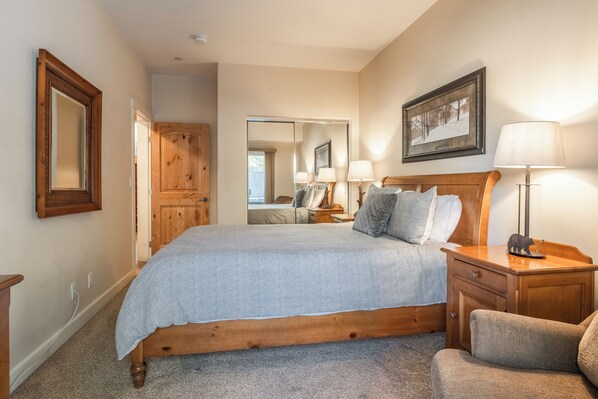 A bedroom with a wooden bed, a nightstand with lamps, a mirror, and a framed picture on the wall.