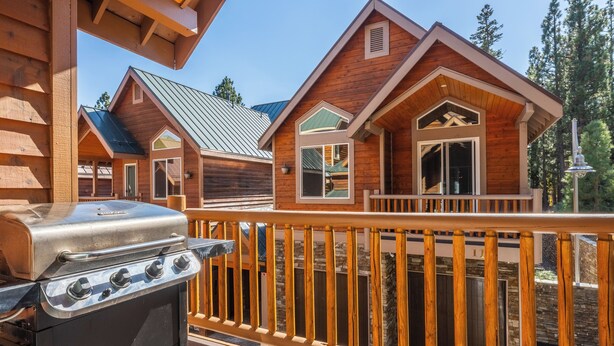 A wooden cabin with a balcony, a grill, and a stone wall. - Mammoth Gateway Village #1 - Updated Townhome-Walk To Village 3 Bed+Loft, Sleeps 10 Private Hot Tub (Mammoth Lakes)