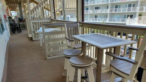 A covered outdoor area with a wooden deck, white plastic chairs, and a table. - Gorgeous 5 Star! Oceanblock Midtown condo directly Across from Convention Center (Ocean City)