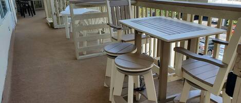 A covered outdoor area with a wooden deck, white plastic chairs, and a table.