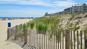 A beach with a wooden fence, beach umbrellas, and a building with multiple balconies. - Gorgeous 5 Star! Oceanblock Midtown condo directly Across from Convention Center (Ocean City)