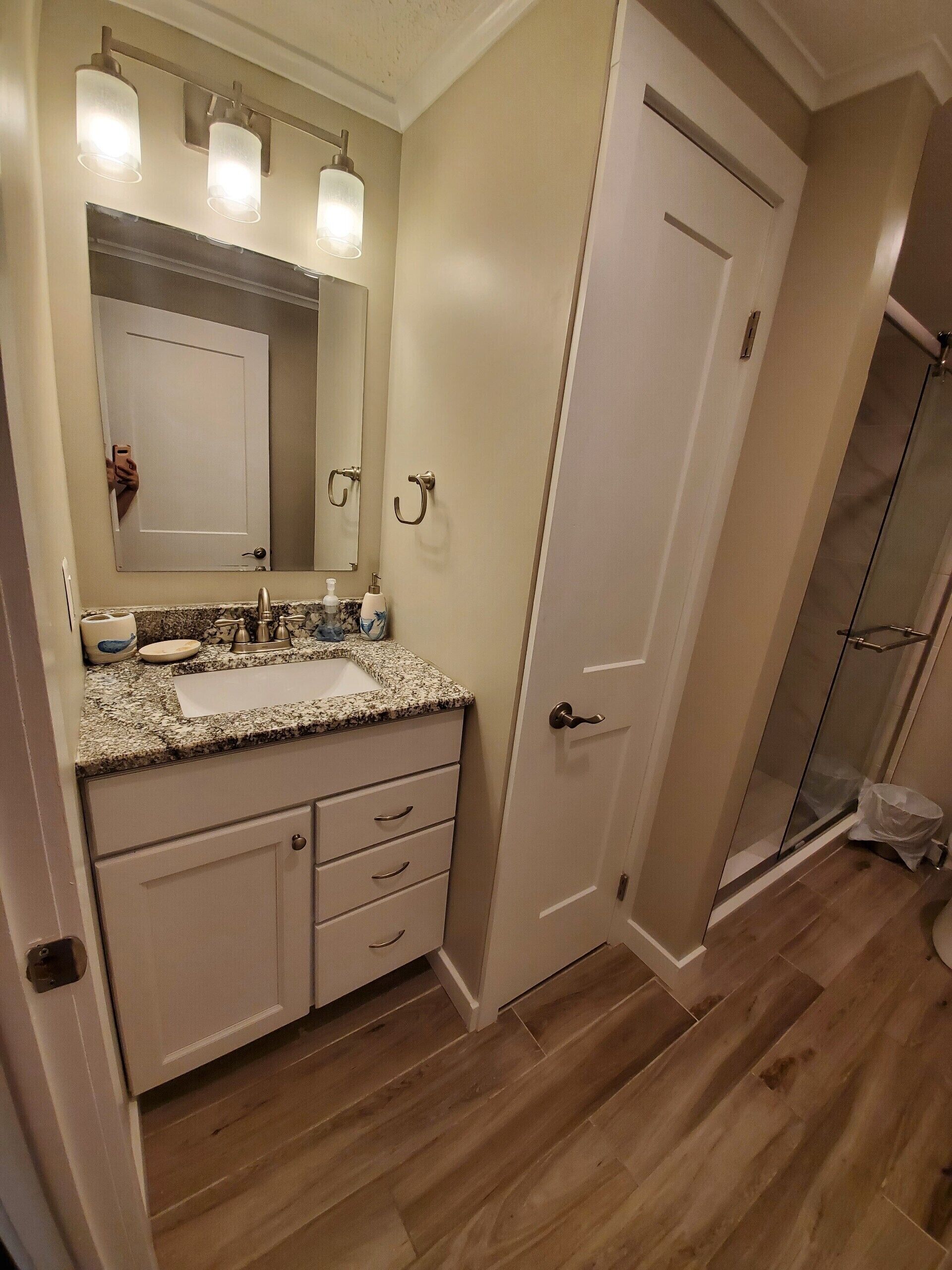 A bathroom with a granite countertop, a mirror, a sink, and a shower area.