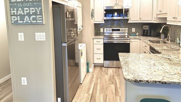 A modern kitchen with white cabinets, stainless steel appliances, a granite countertop, and a green stool. - Gorgeous 5 Star! Oceanblock Midtown condo directly Across from Convention Center (Ocean City)