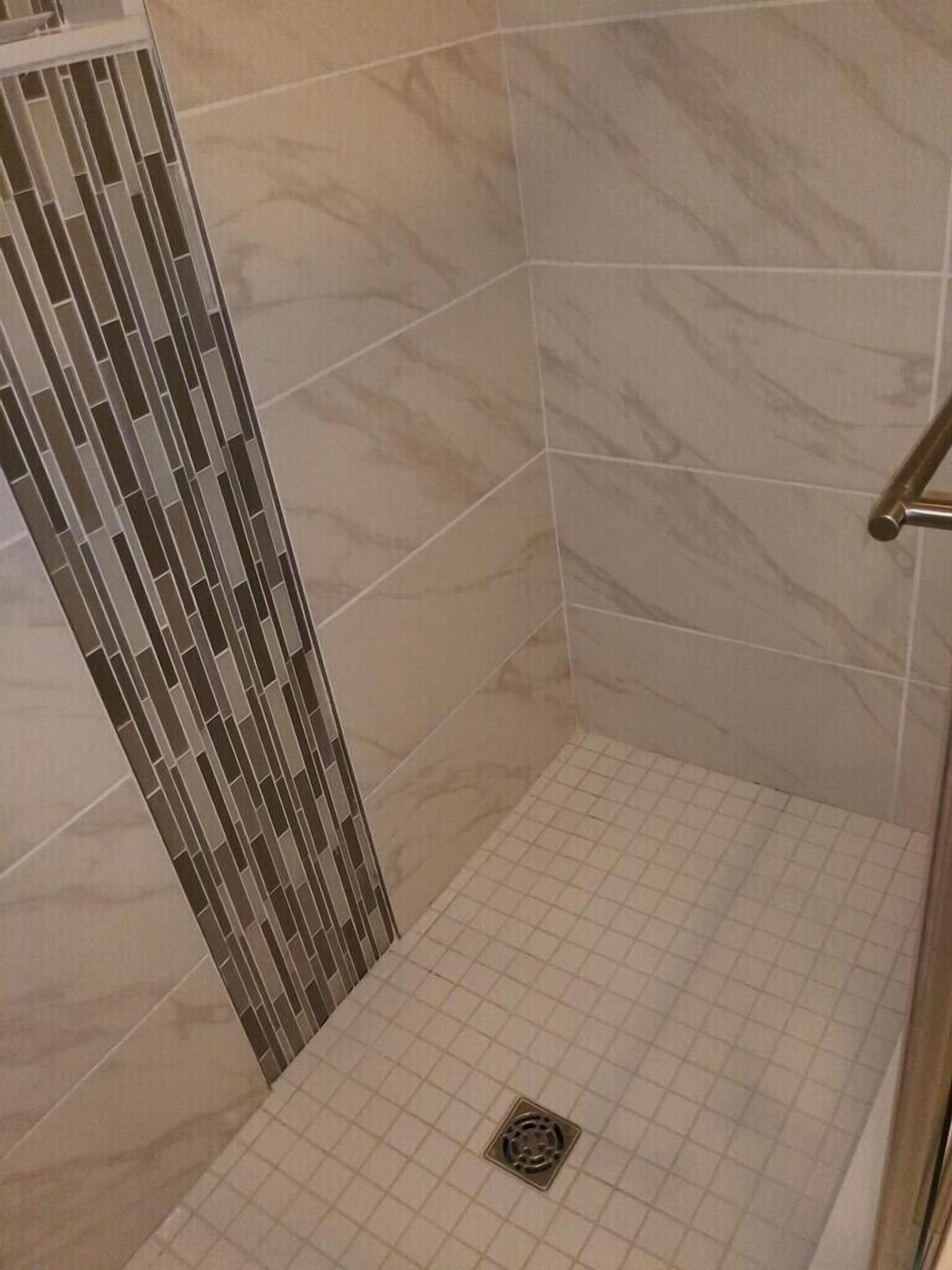 Een douche met betegelde vloer en een verticale wand met rasterpatroon.