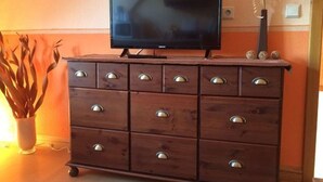 Un aparador de madera con un televisor de pantalla plana encima, un florero con plantas secas y un interruptor de pared.
