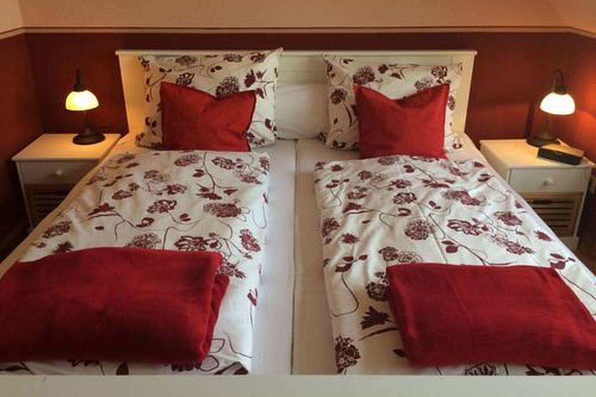 A twin bed with floral bedding and red pillows in a room with a sloped ceiling and two bedside lamps.