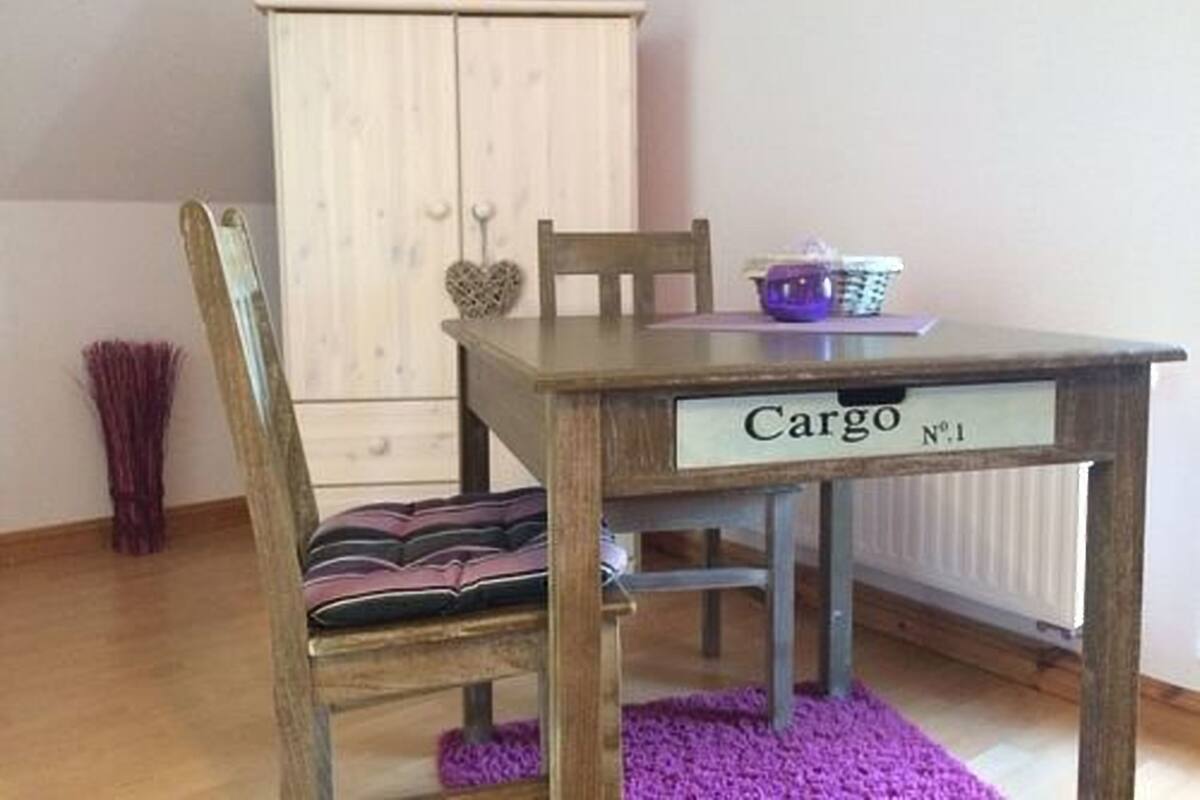 A dining table with a 'Cargo' sign, two chairs, a purple rug, and a white cabinet with heart-shaped decorations.