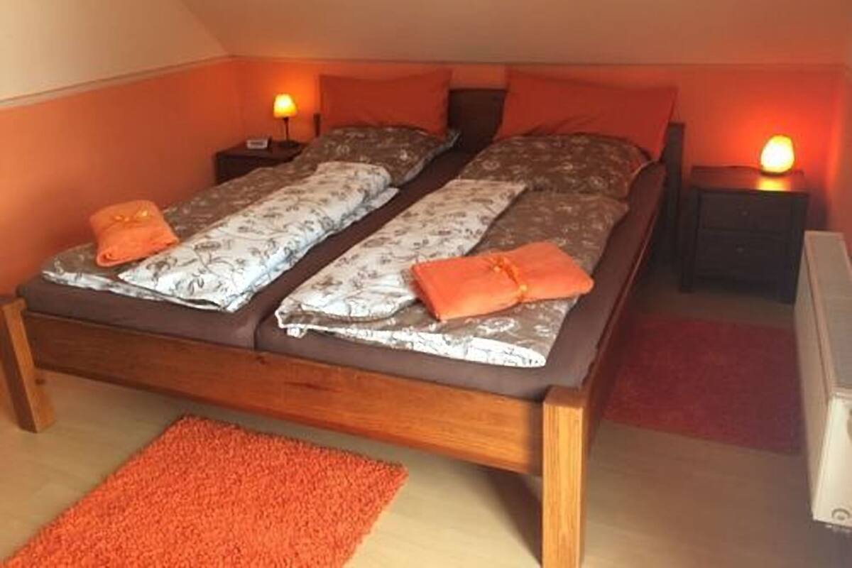 A double bed with patterned bedding, two bedside tables with lamps, and a red carpet.