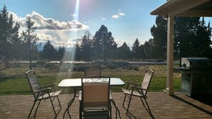 Un patio con una mesa y sillas, una parrilla y vistas a un parque con árboles y una carretera.