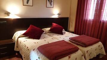 Habitación de hotel con una cama grande, dos almohadas rojas, una colcha blanca acolchada y dos lámparas de pared.