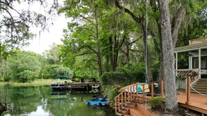Un muelle de madera se extiende sobre un río tranquilo, rodeado de abundante vegetación y árboles.