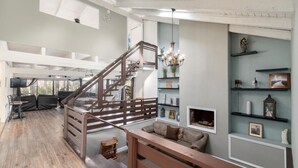 Un salón amplio con una escalera de madera, un candelabro y estantes con objetos decorativos.