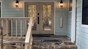 Una casa con una escalera de piedra que lleva a una puerta con paneles de vidrio decorativos y un letrero de bienvenida.