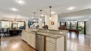 Una cocina amplia con una isla central, suelo de madera e iluminación colgante.