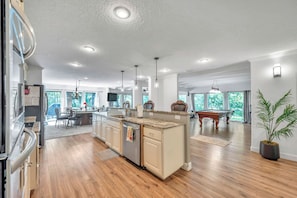 A spacious kitchen with a central island, wooden flooring, and a dining area with a pool table.
