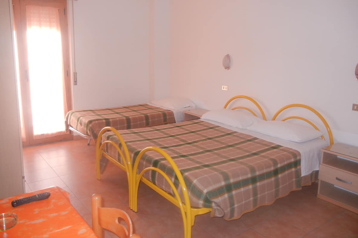 Una habitación con dos camas, una mesita con un control remoto y una silla.