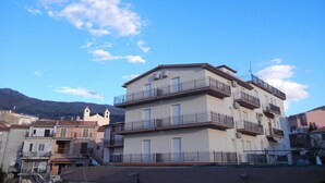 Un edificio residencial de varios pisos con balcones, unidades de aire acondicionado y monta ñas al fondo.