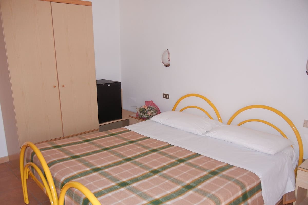 Un dormitorio con cama, armario, una mesita y televisor.