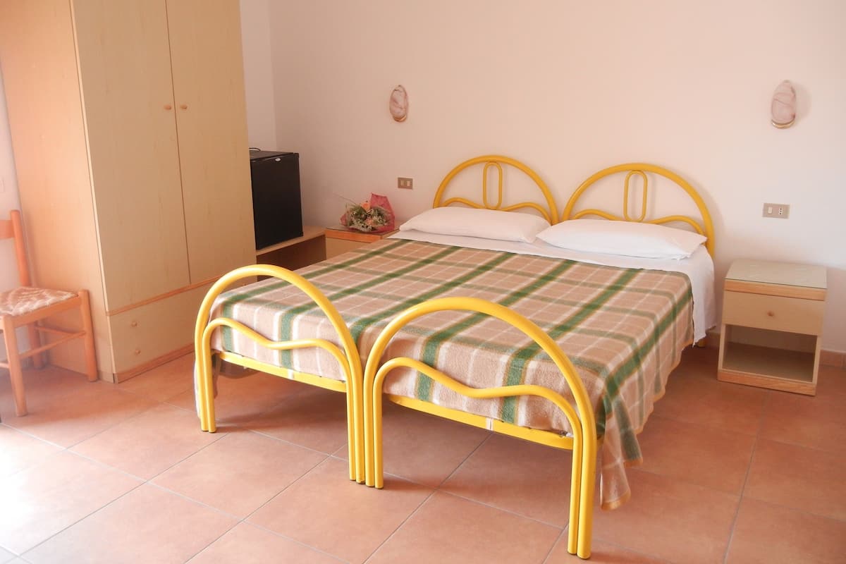Un dormitorio con una cama, un armario, una silla, una mesita de noche y una pequeña mesa con una lámpara.