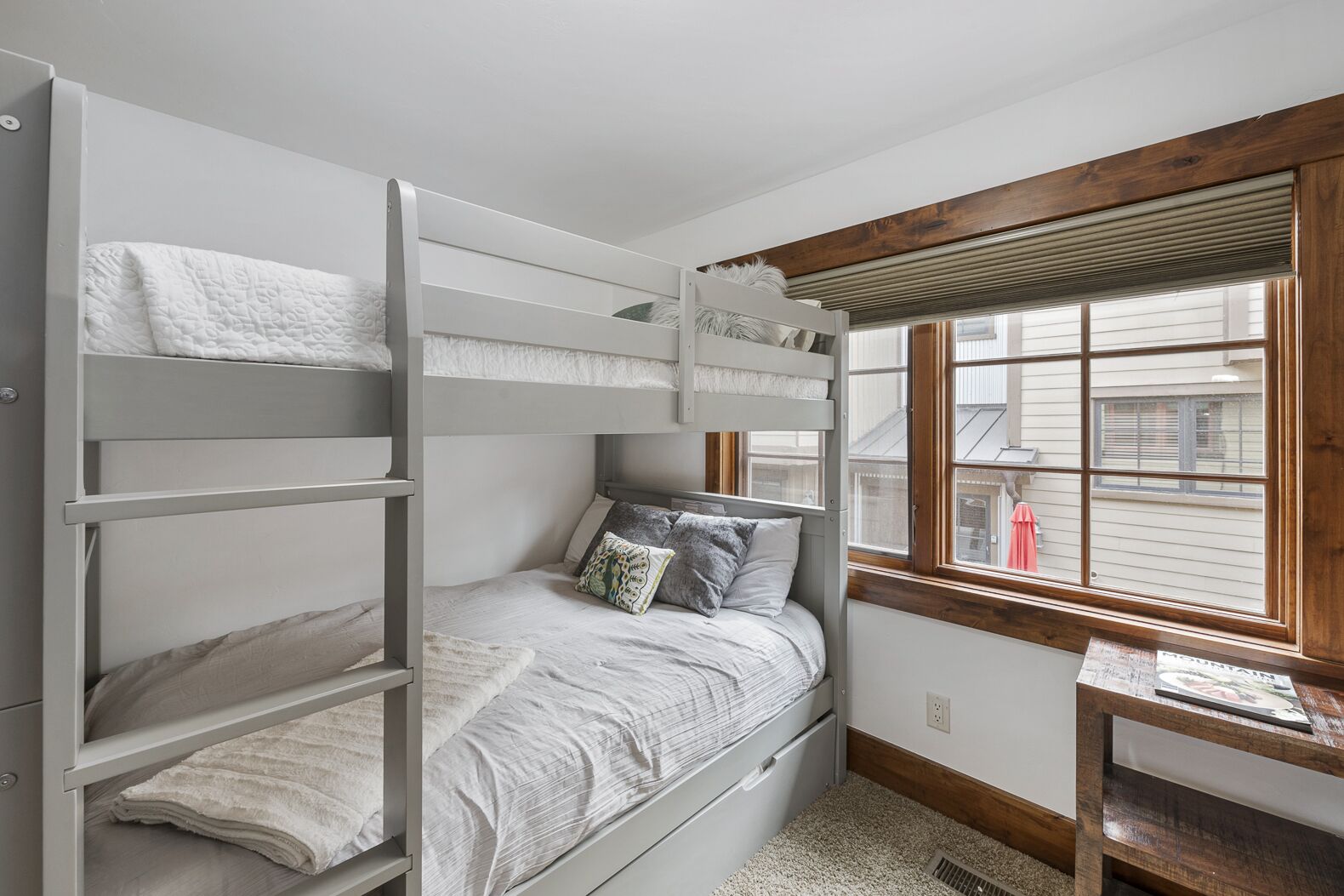 A bunk bed room with a window and a small wooden table.