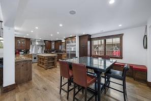 Une cuisine spacieuse dotée d’un îlot central, de meubles en bois, d’appareils électroménagers en acier inoxydable et d’un coin repas avec une table en verre et des chaises en cuir.