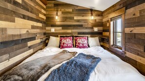 Una camera da letto con una parete in legno a tronchi, un letto grande con biancheria bianca, due cuscini rossi e una coperta di pelliccia.