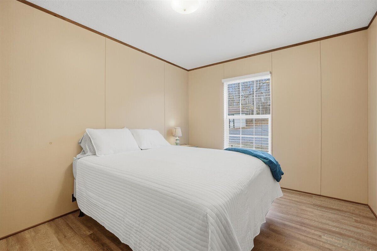 A bedroom with a bed, a window with blinds, and a nightstand with a lamp.