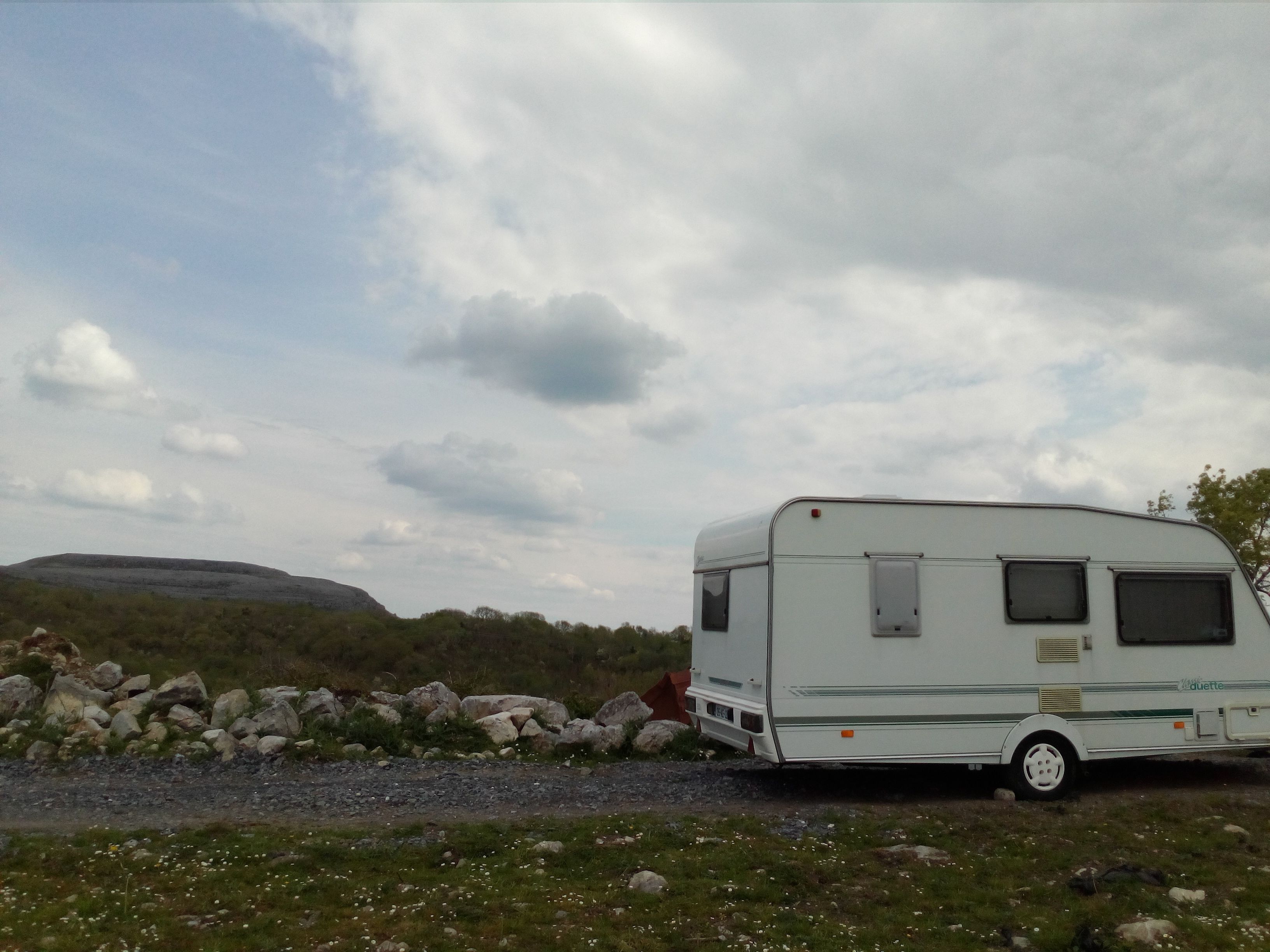 A white RV parked on a gravel path with a rocky landscape and hills in the background.