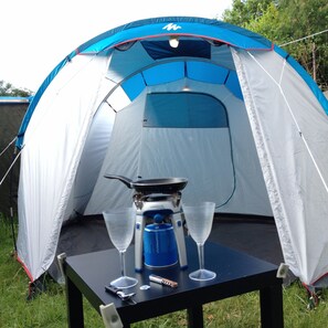 Een koepelvormige tent met een tafel ervoor, een draagbaar fornuis en twee glaasjes.