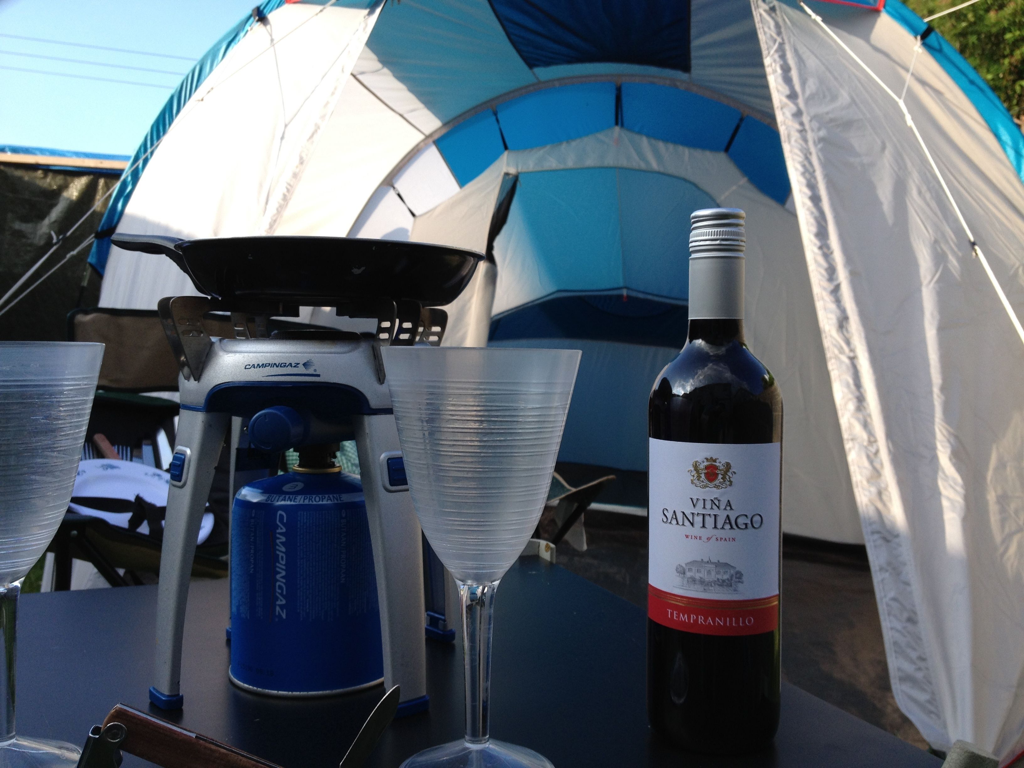A camping setup with a tent, a portable stove, a wine bottle, and a glass.