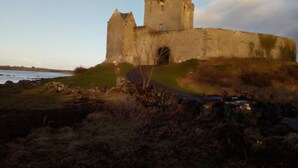 A historic castle with a large tower and a fortified wall, situated on a grassy hill overlooking a body of water. - Burren Bushcraft - Camping & Adventures (Carran)