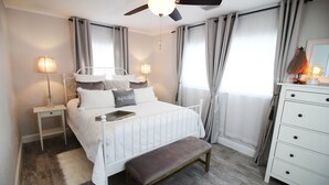 Une chambre à coucher comprenant un lit, des tables de chevet, un banc, une commode et un ventilateur de plafond.