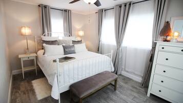 Une chambre à coucher comprenant un lit, des tables de chevet, un banc, une commode et un ventilateur de plafond.