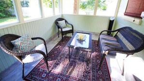 Une véranda meublée de mobilier en osier, agrémentée d’un tapis à motifs et offrant une vue sur l’extérieur.