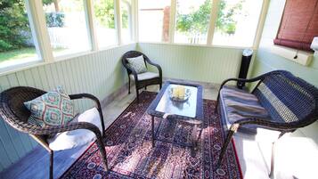 Une véranda meublée de mobilier en osier, agrémentée d’un tapis à motifs et offrant une vue sur l’extérieur.