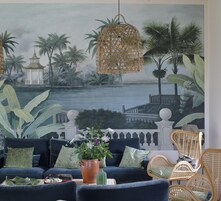 A living room with a mural of a tropical scene, a blue sofa, wicker chairs, and a potted plant.