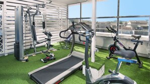 Un gimnasio con cinta de correr, elíptica y bicicleta estática, que cuenta con piso de césped artificial verde y ventanas amplias.