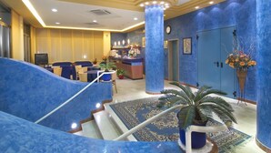 Un vestíbulo de hotel con alfombra azul, un mostrador de recepción y una escalera.