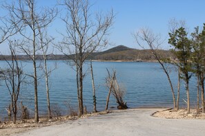A clear view of a lake with a dirt path leading to the water, surrounded by leafless trees and a distant hill. - Lakefront - Gentle Slope to Water - Sleeps 18 (Shell Knob)