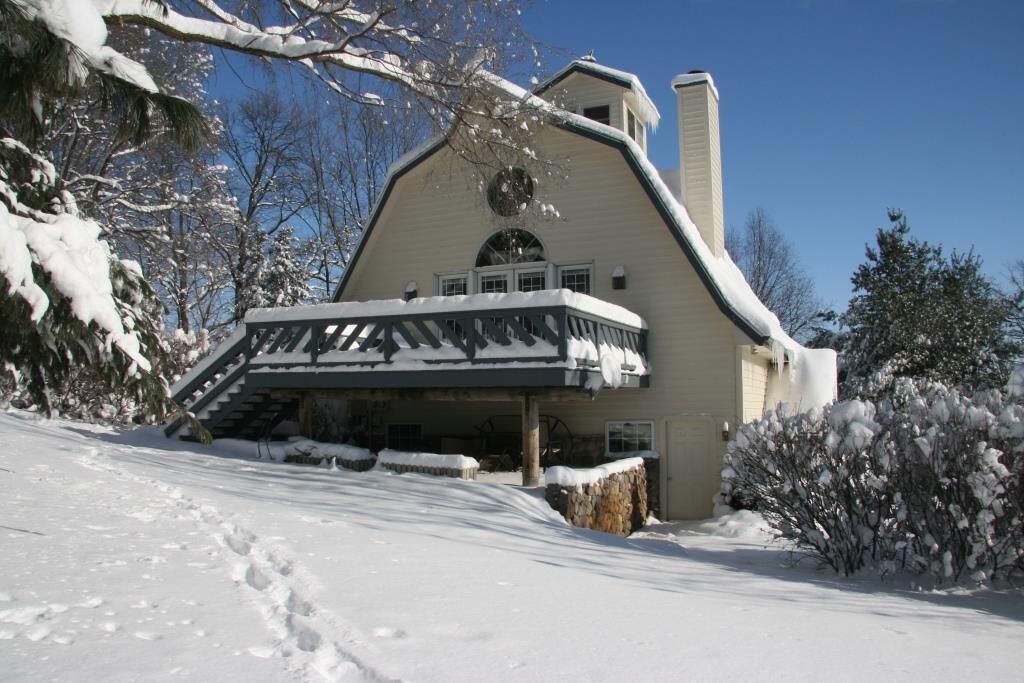 A snow-covered house with a large porch and a chimney.