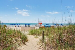 Ein Strandweg führt zum Meer, mit Strandliegen und einem Rettungsturm.