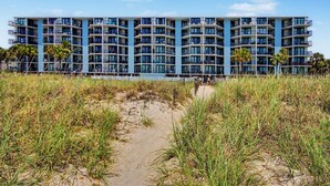 A multi-story hotel with balconies, a sandy beach in the foreground, and palm trees. - Oceanfront Two Bedroom Condo - Crescent Sands H-5 (North Myrtle Beach)