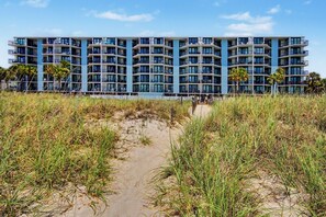 A multi-story hotel with balconies, a sandy beach in the foreground, and palm trees. - Oceanfront Two Bedroom Condo - Crescent Sands H-5 (North Myrtle Beach)