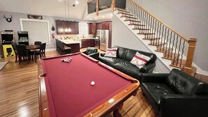 Ein Wohnzimmer mit Billardtisch, einer schwarzen Ledersofa und einer Treppe zu einer oberen Ebene.