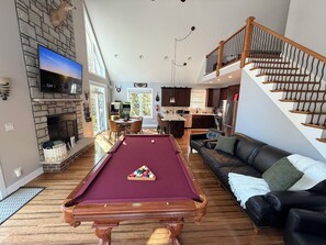 Un grand espace de vie comprenant une table de billard, un canapé confortable, une cuisine et un escalier.