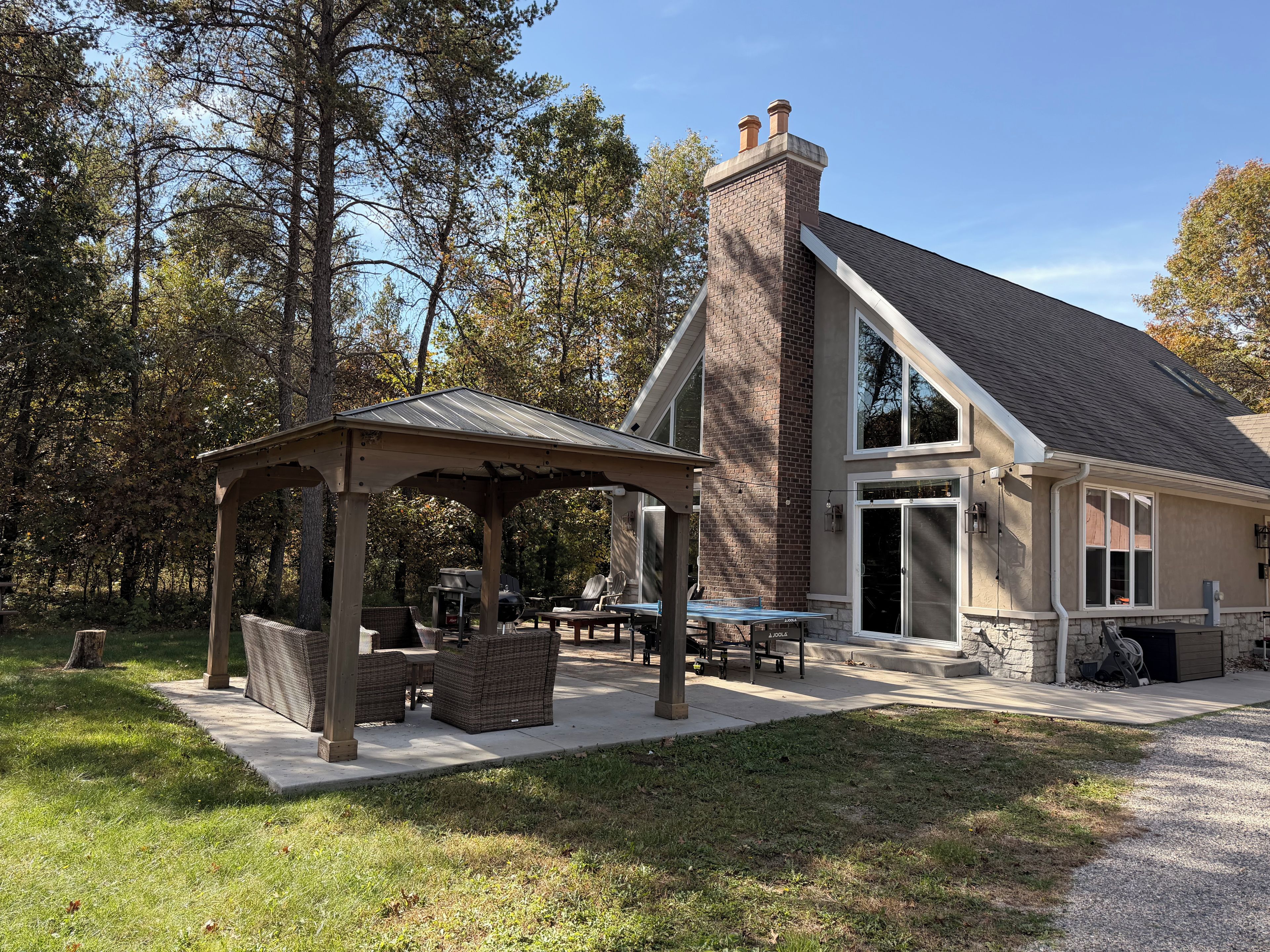 A house with a covered patio, outdoor furniture, and a stone fireplace.