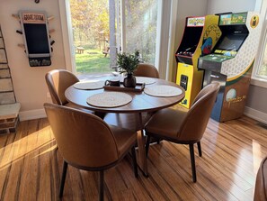 Ein Essbereich mit einem runden Tisch, vier Stühlen und Blick auf eine Golf-Spielautomat.