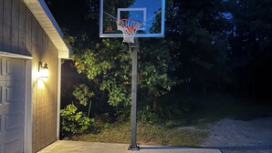 Ein Basketballkorb in einer Wohngegend, mit Garage und Bäumen im Hintergrund.